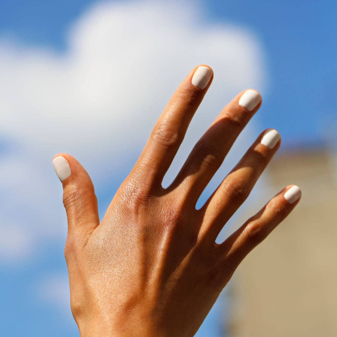 Hand with white nail polish against a blurred blue sky background