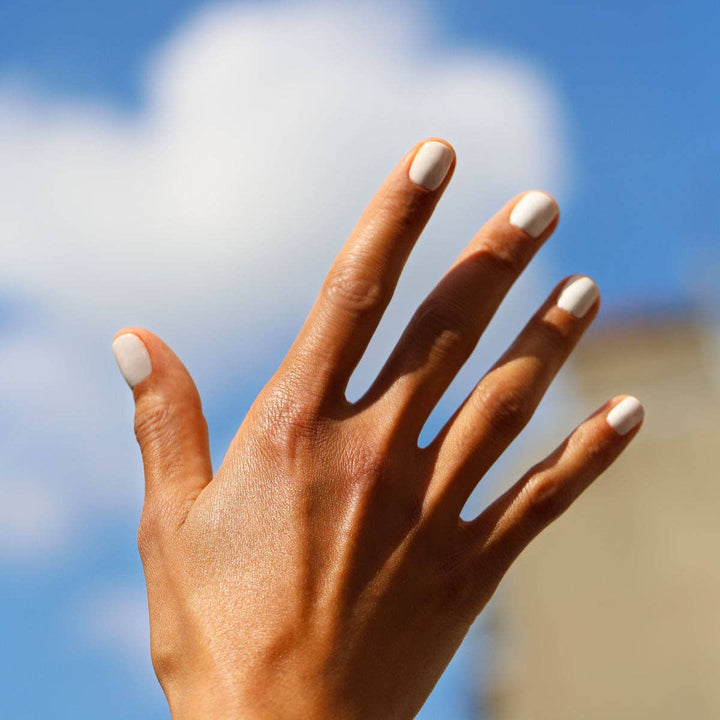 Hand with white nail polish against a blurred blue sky background