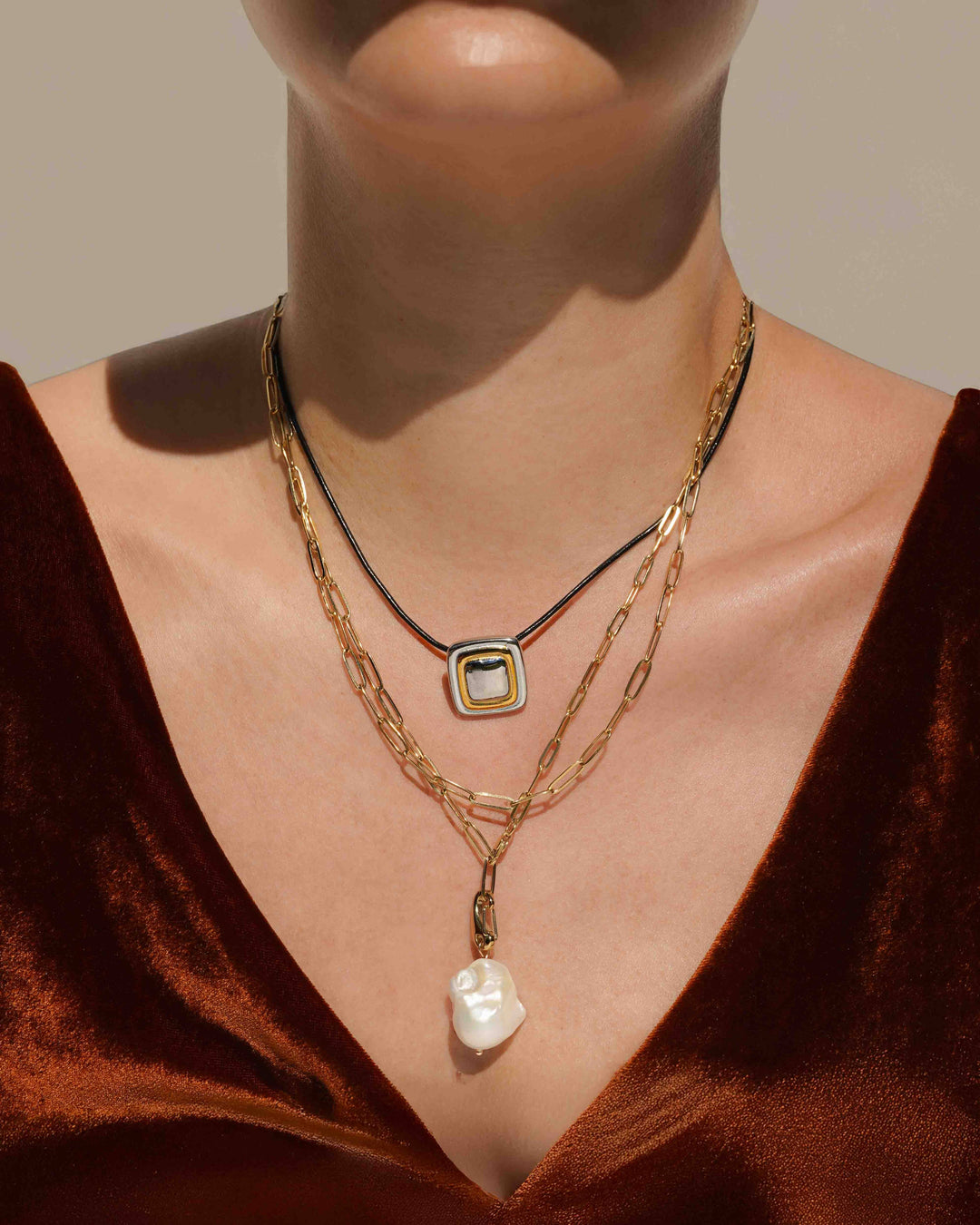 Necklace with a square pendant and pearl on a person wearing a brown velvet garment.