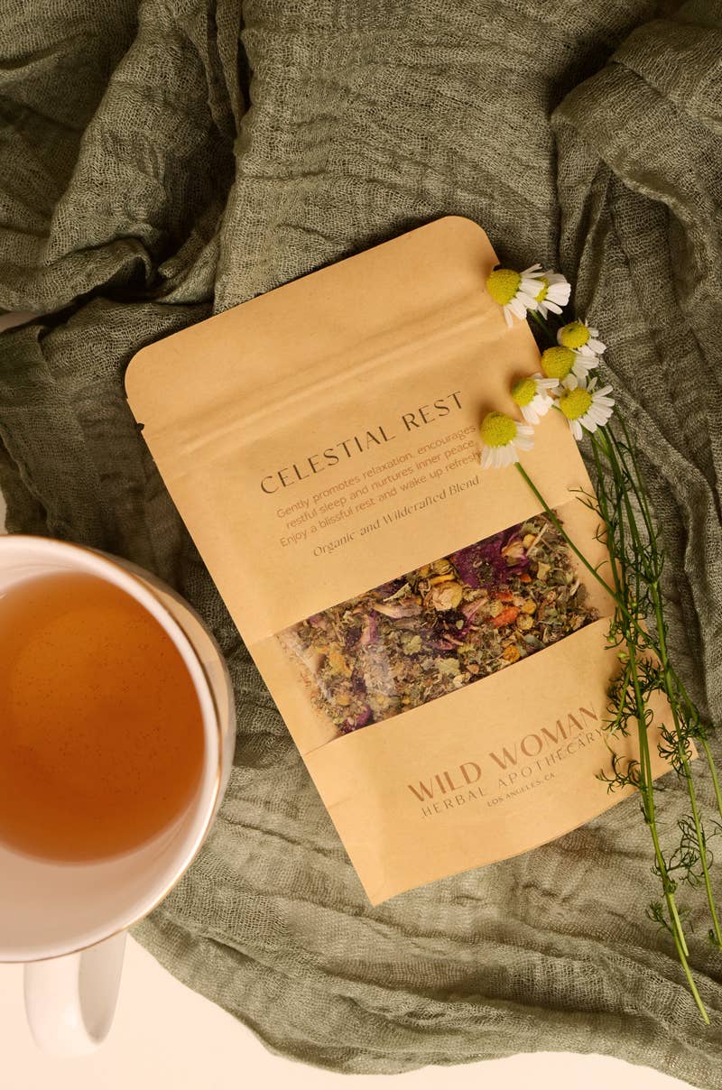 Bag of'Celestial Rest' from 'Wild Woman Herbs with a cup of tea and flowers on a green fabric background.