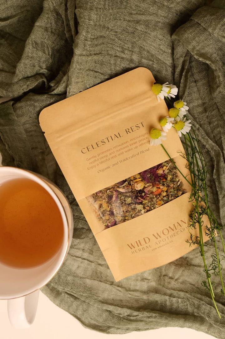 Bag of'Celestial Rest' from 'Wild Woman Herbs with a cup of tea and flowers on a green fabric background.