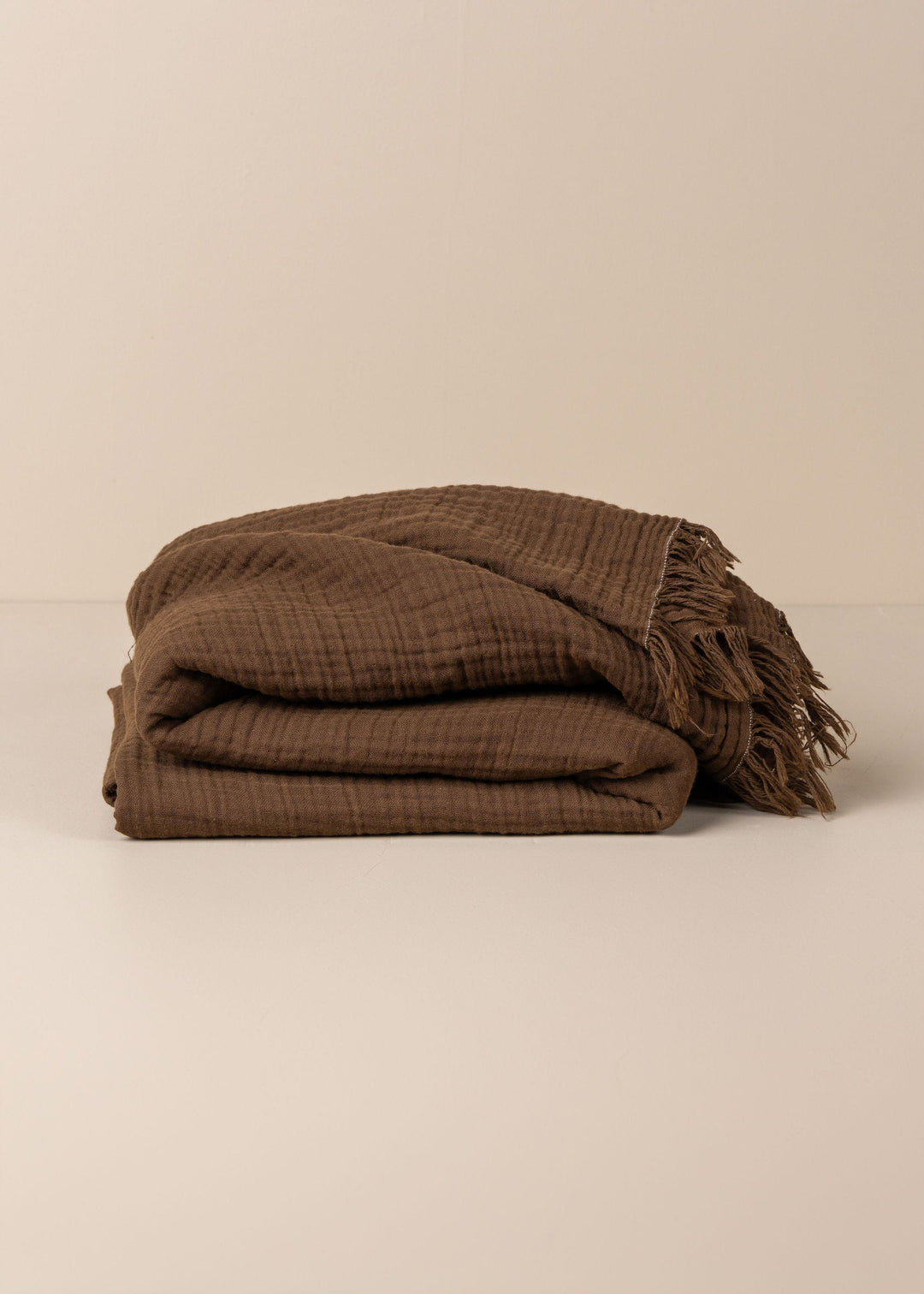 Brown textured blanket with fringes on a beige background