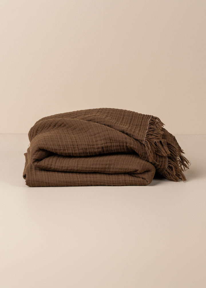 Brown textured blanket with fringes on a beige background