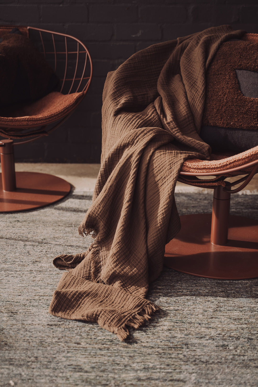 Brown textured blanket draped over a chair with a dark brick wall in the background