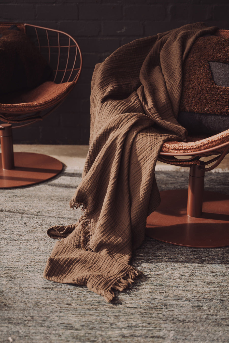 Brown textured blanket draped over a chair with a dark brick wall in the background