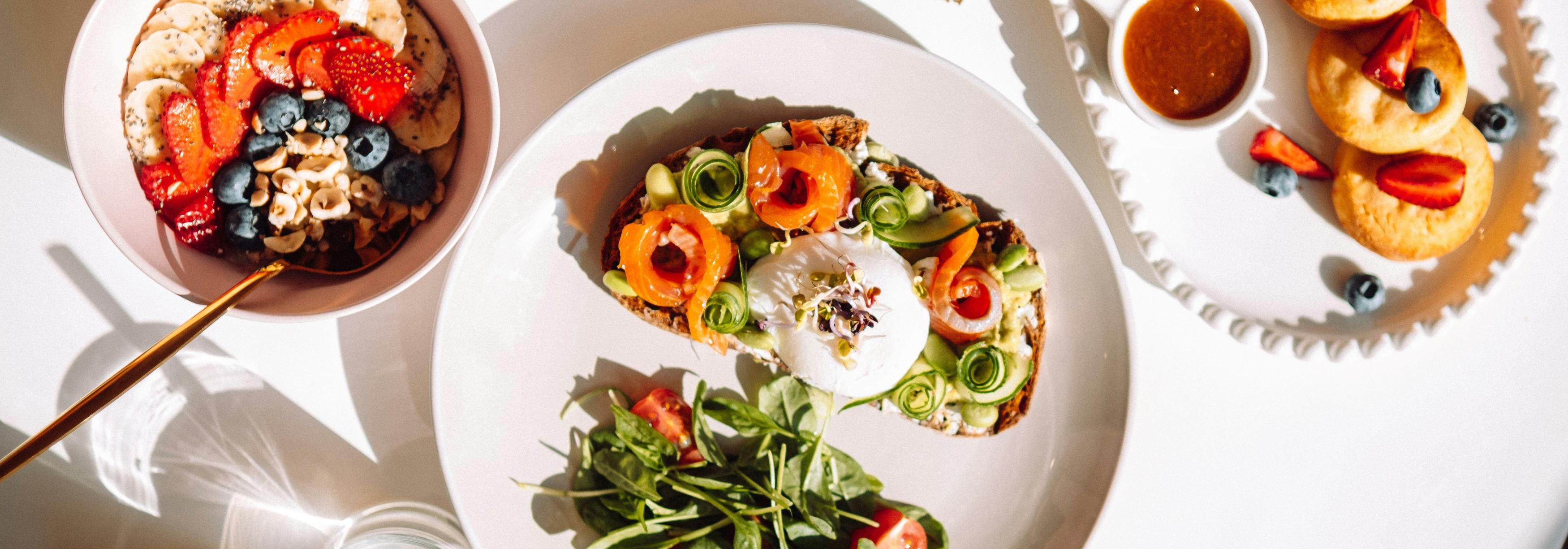 A flatlay image of healthy dishes including salmon burrata toast, a fruit bowl, and more