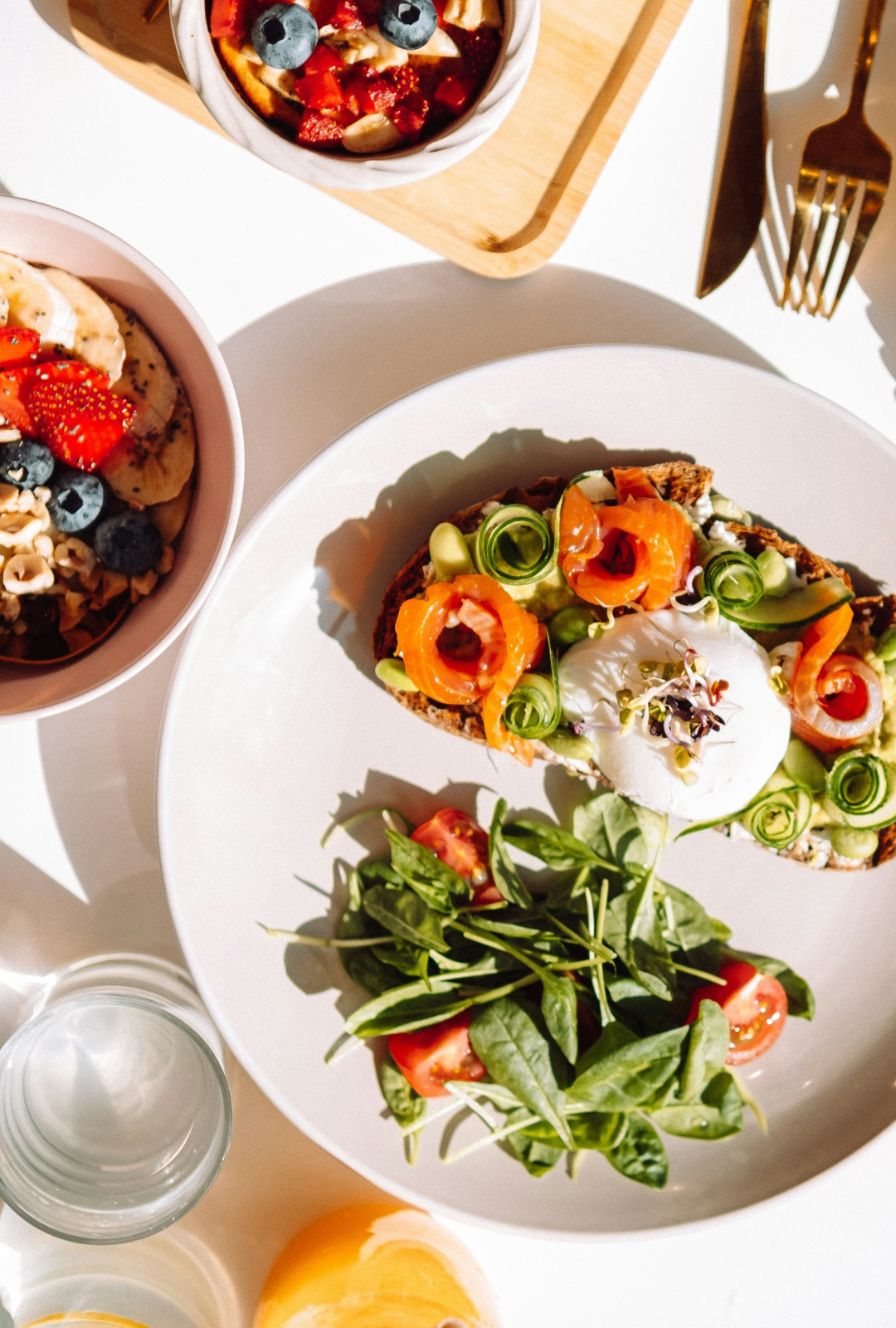 A flatlay image of healthy dishes including salmon burrata toast, a fruit bowl, and more