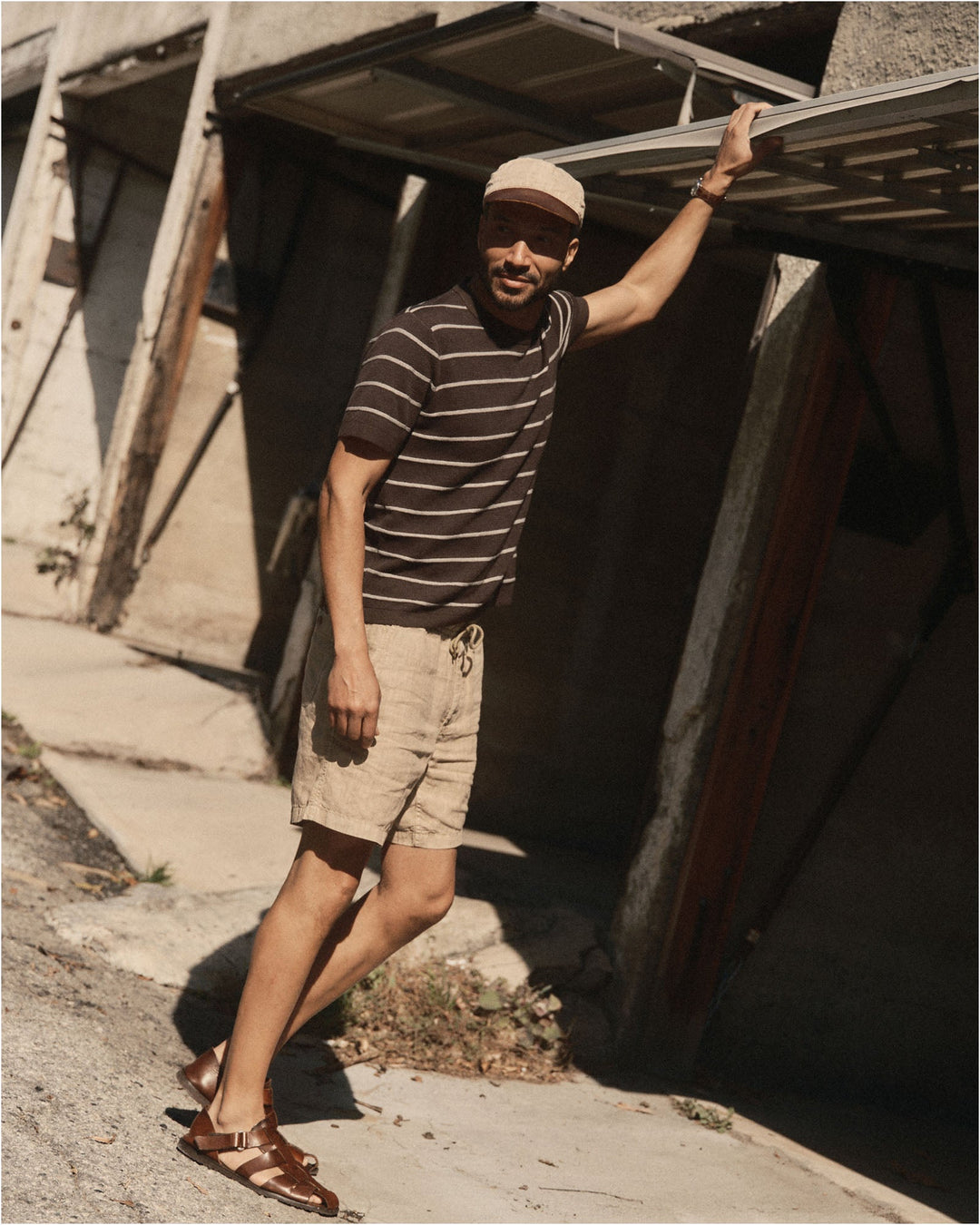 Man standing outside a small building wearing The Brody Sweater Tee in Espresso Stripe and beige shorts.