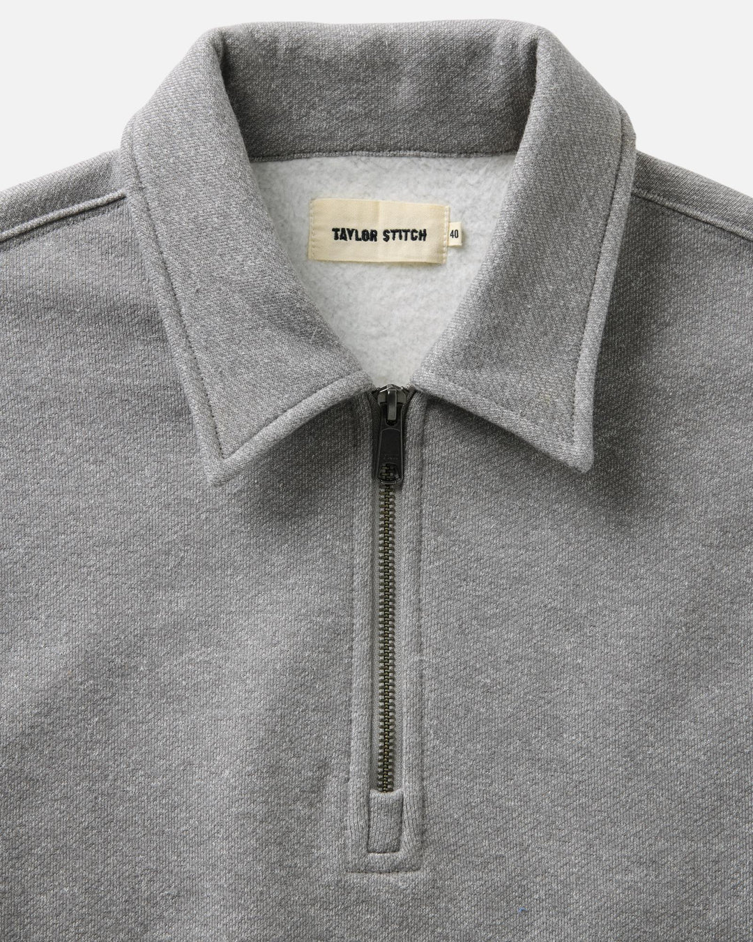 Close-up of a heather gray quarter-zip sweatshirt collar with a visible neck label reading Taylor Stitch.