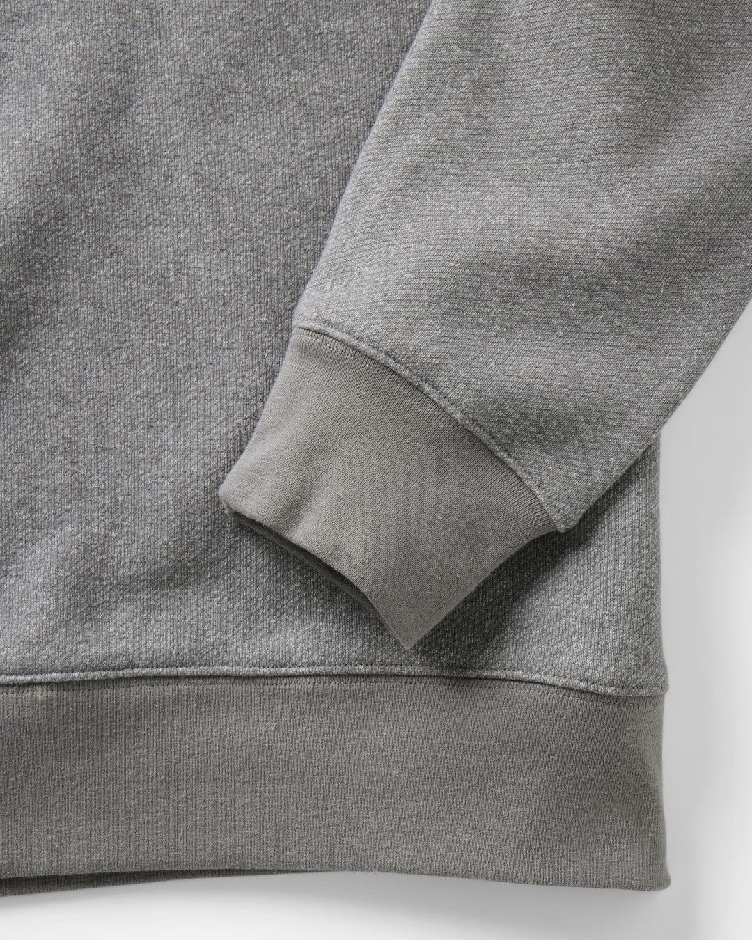 Close-up of a heather gray sweatshirt showing the ribbed cuff and hem of the sleeve, with a matching gray body and clean studio background.
