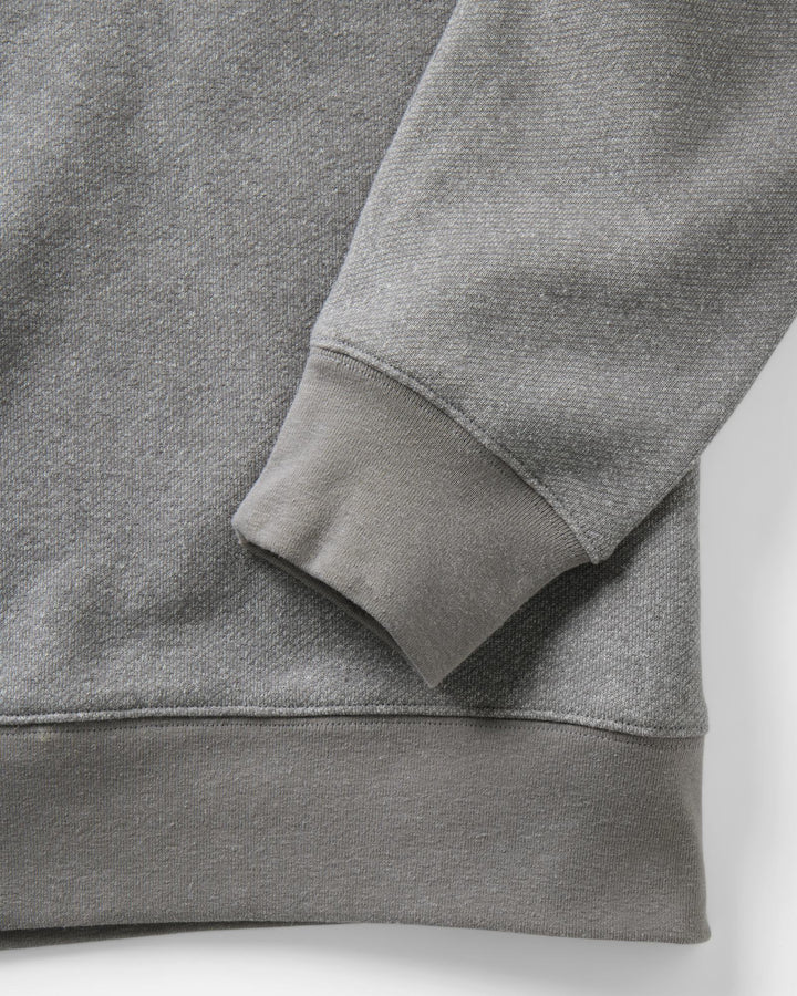 Close-up of a heather gray sweatshirt showing the ribbed cuff and hem of the sleeve, with a matching gray body and clean studio background.