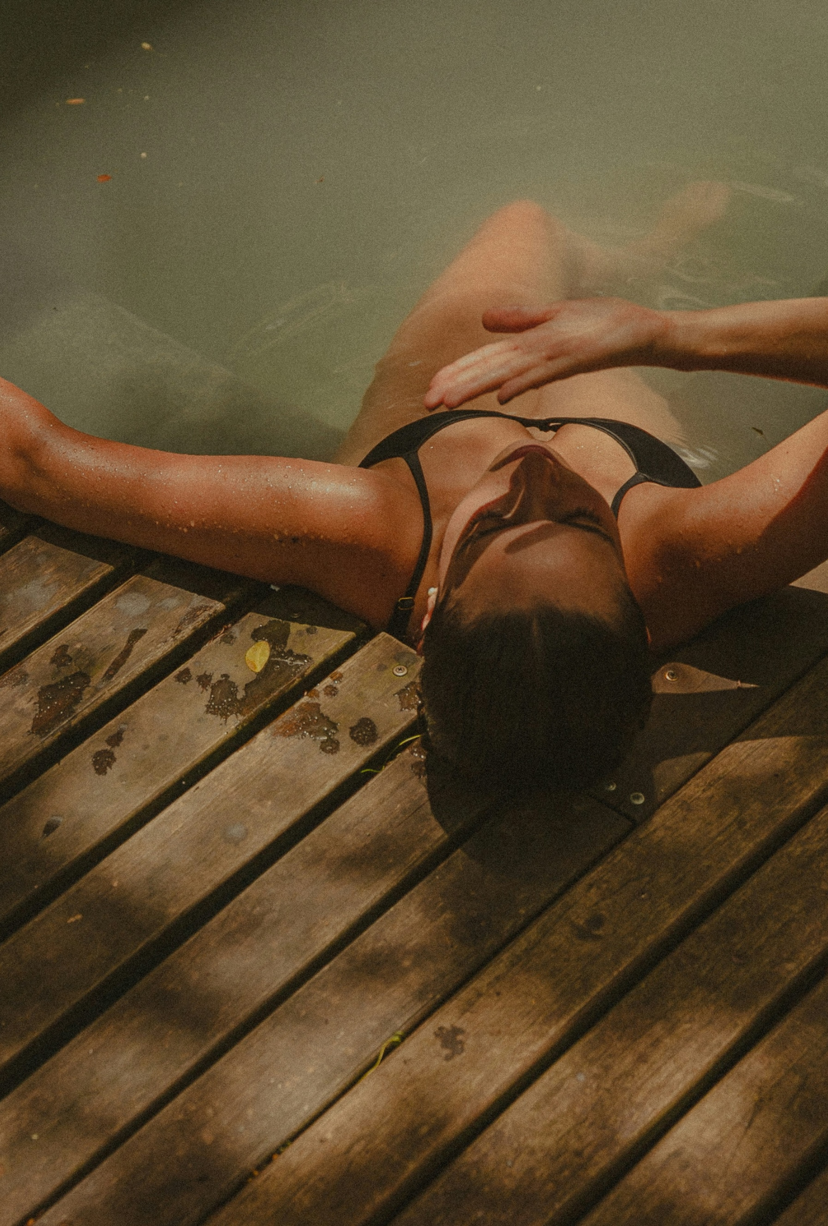 A woman wearing a black bikini sitting in a pool holding her hand up to shade her face