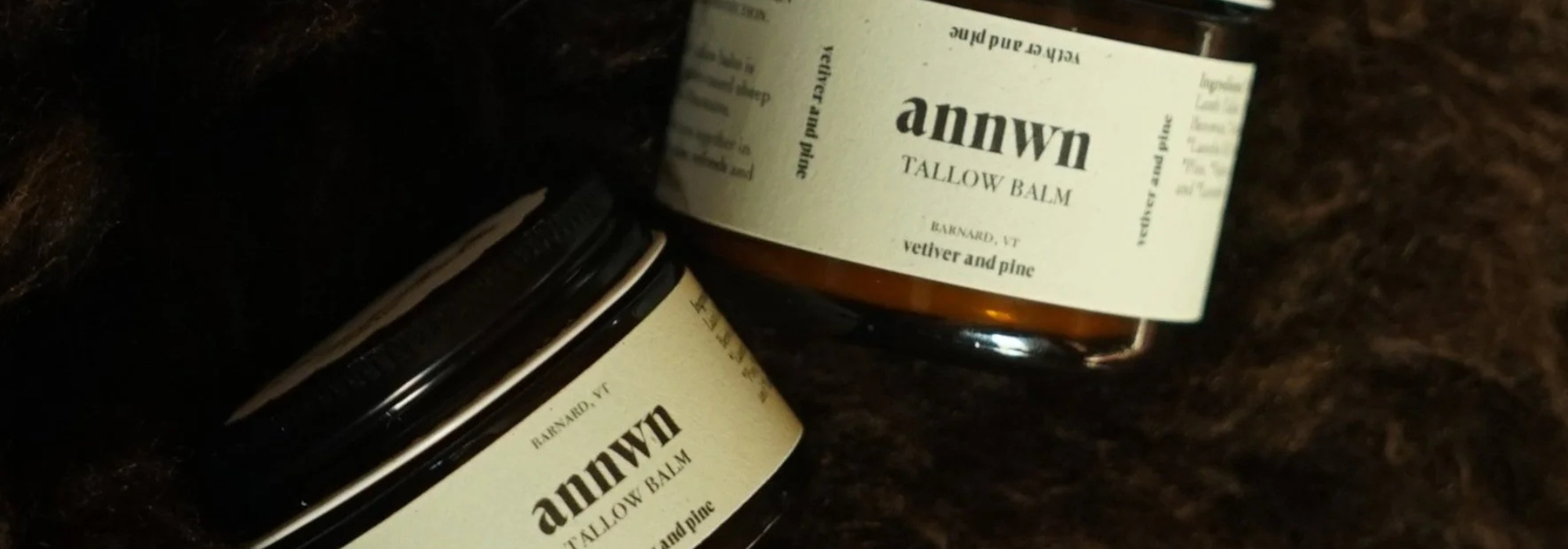 Two jars of Annwn Tallow balm on a textured surface
