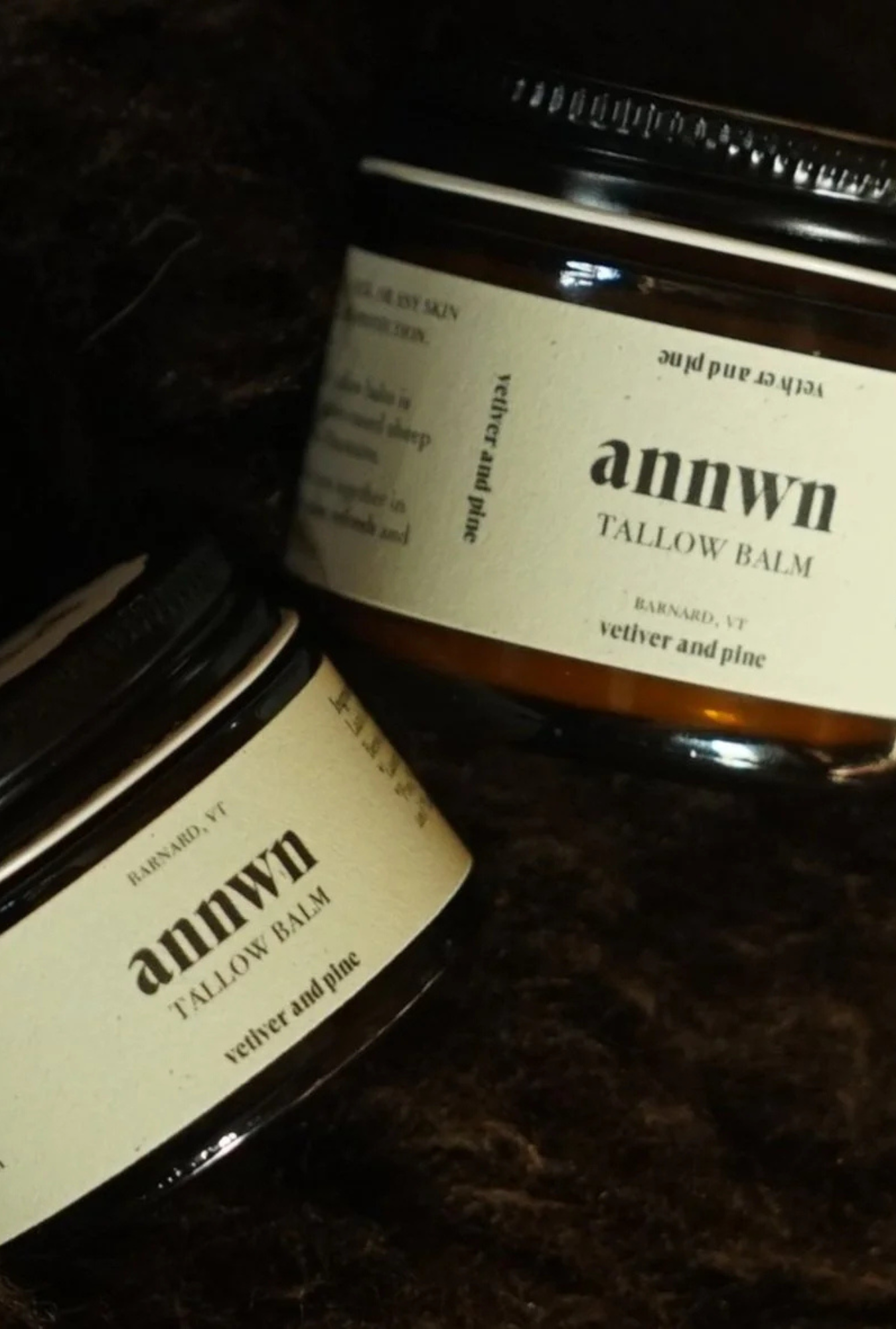 Two jars of annwn tallow balm on a dark textured surface