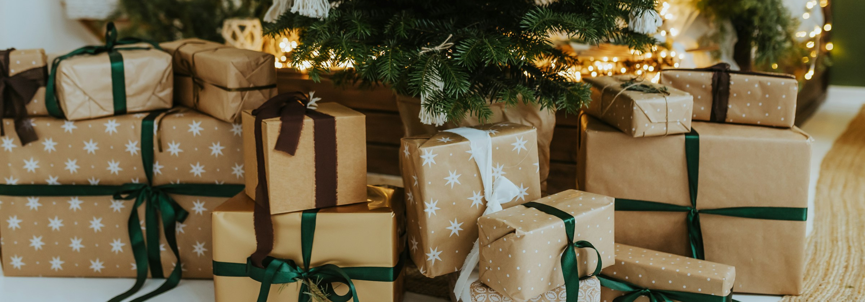 Gift boxes wrapped in brown paper with green ribbons under a decorated Christmas tree.