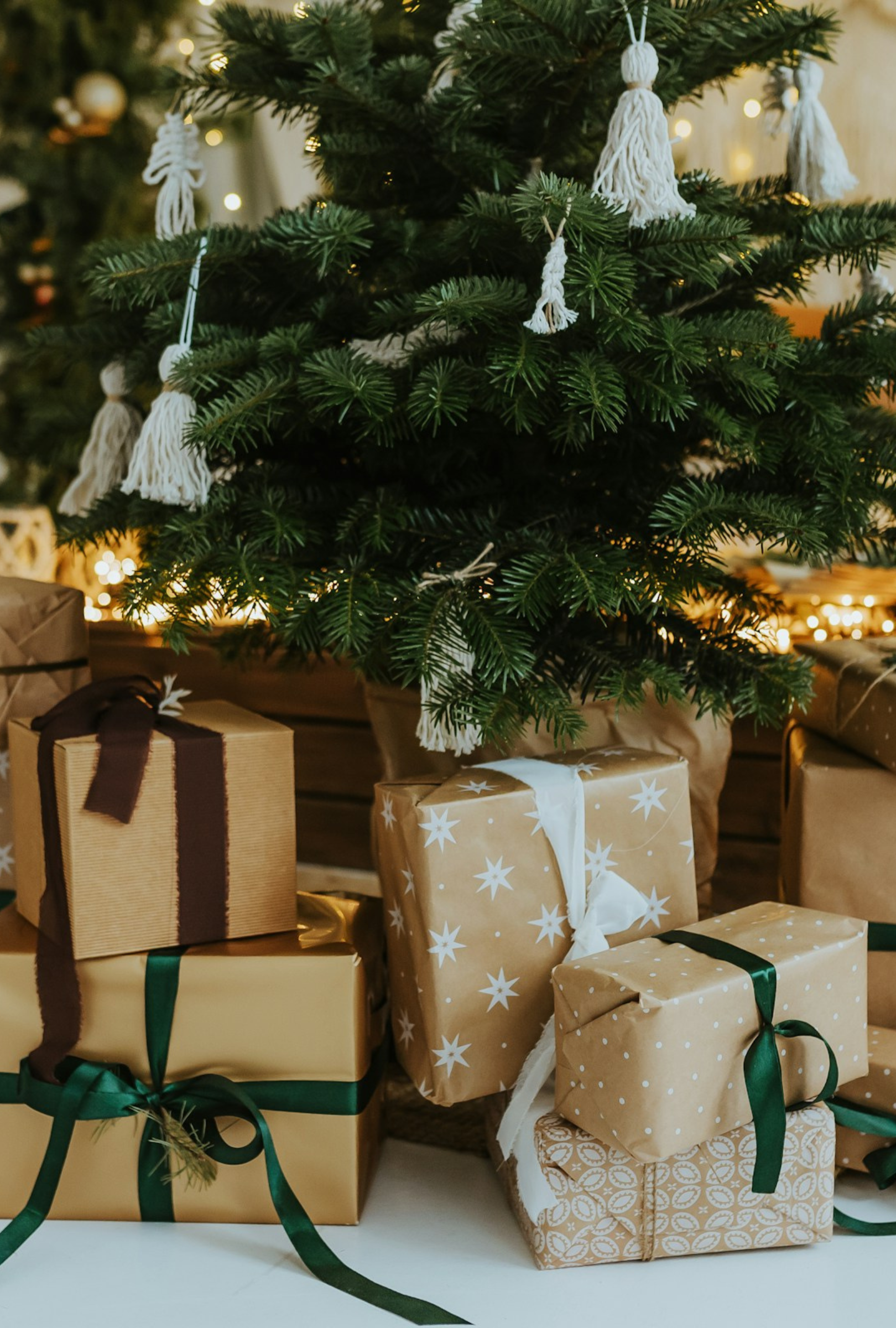 Christmas tree with wrapped gifts in brown kraft paper and green, brown and white ribbon underneath