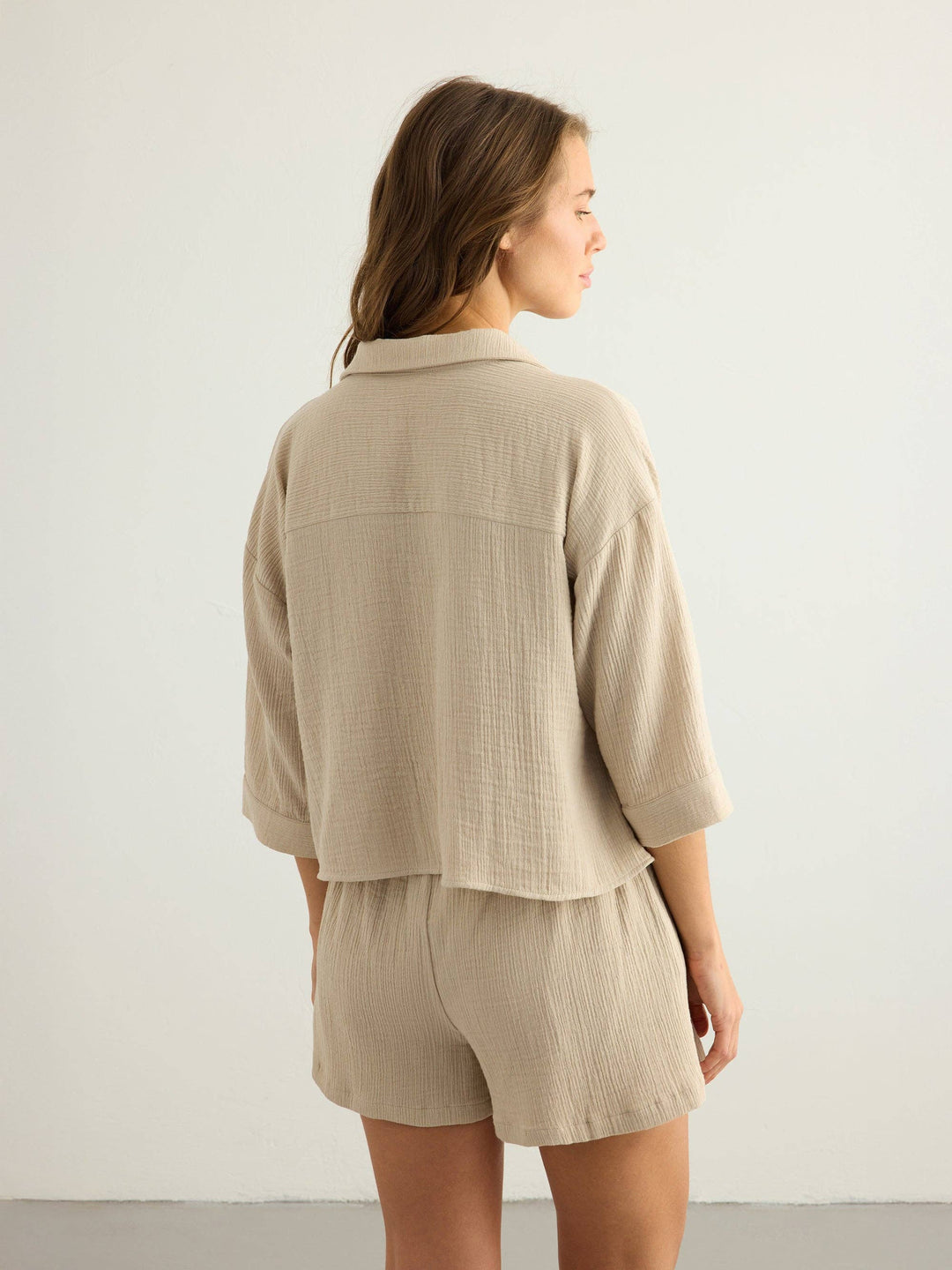 Woman wearing a Handloom Aura oatmeal button-up shirt and shorts from behind on a plain background