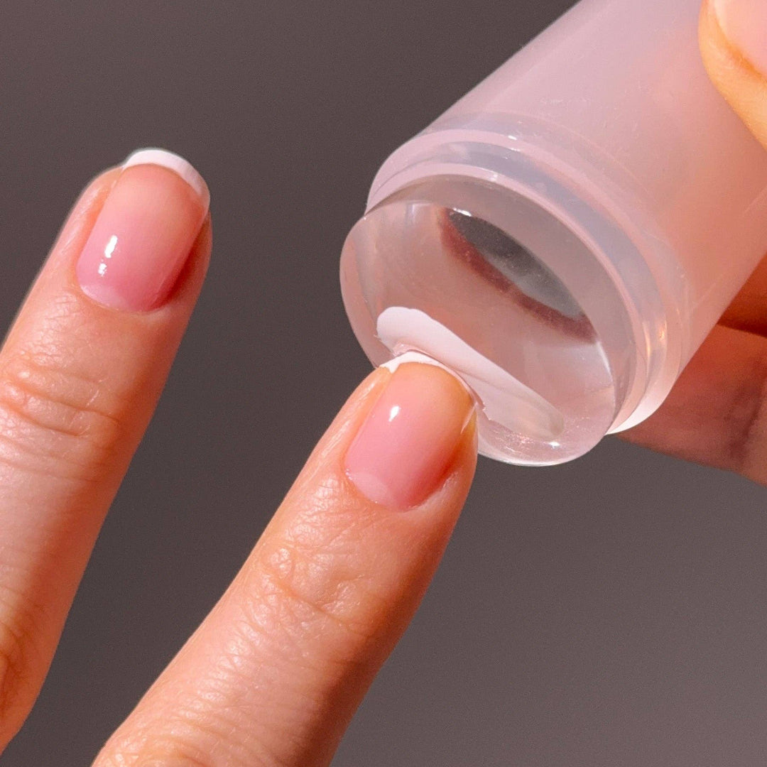 Close-up of a hand using the mani stamp to a fingernail against a dark background