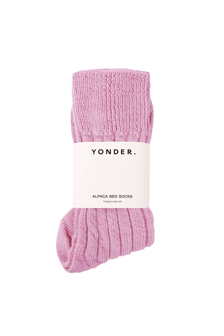 A pair of pink alpaca bed socks with a ribbed knit texture, wrapped in a white paper band labeled &