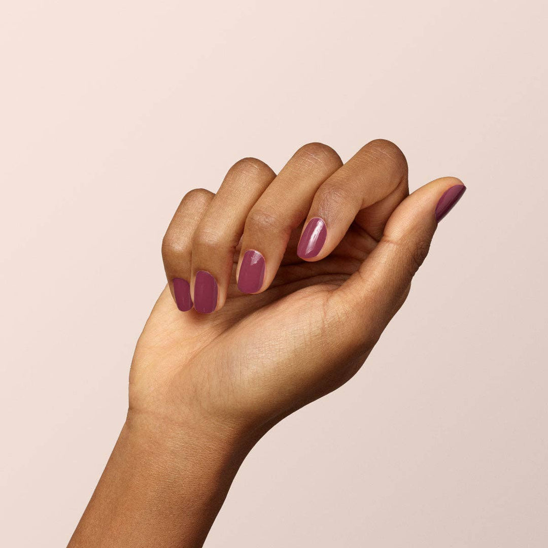 Hand with Victoria Plum nail polish on a beige background