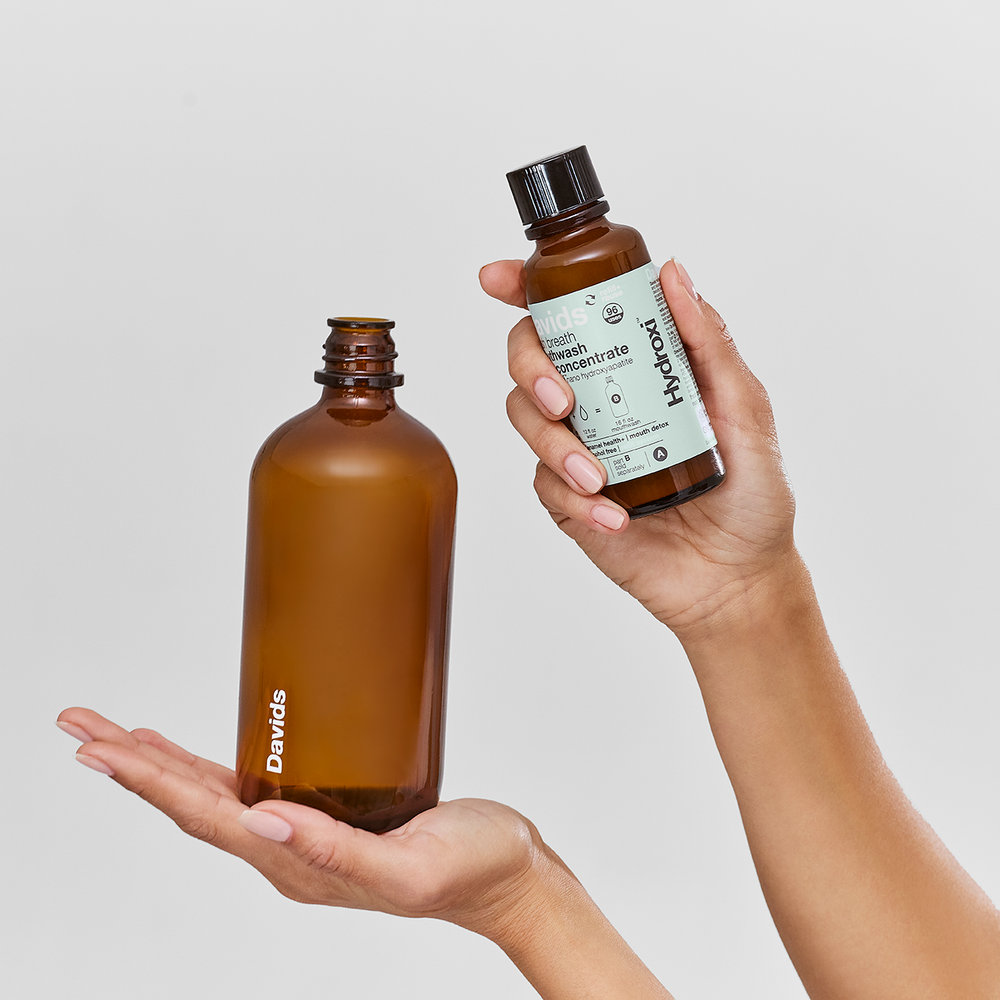 Two brown bottles, one labeled 'Davids' and the other 'Hydroxil,' held by a person against a light gray background.