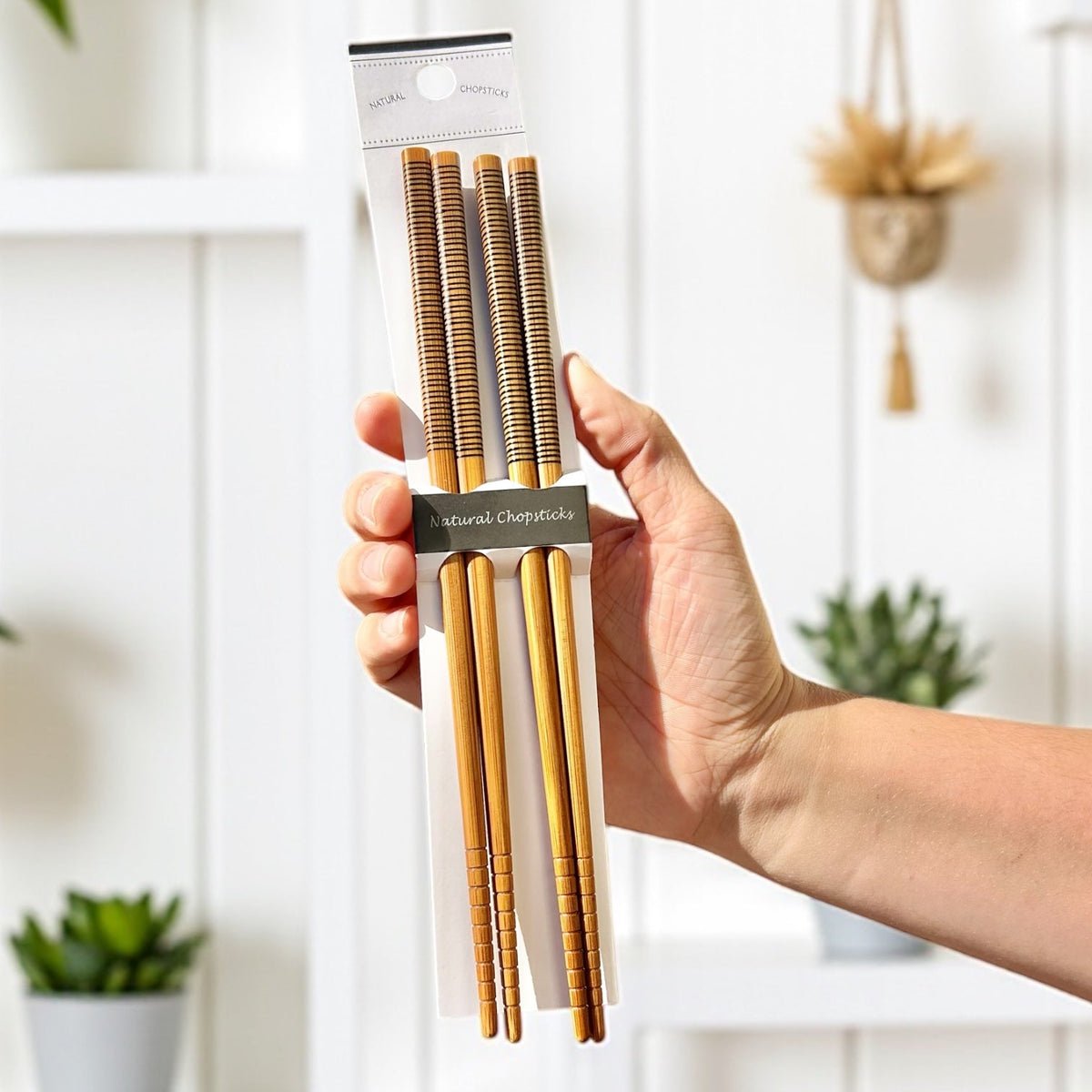 Hand holding a package of bamboo chopsticks with a white background
