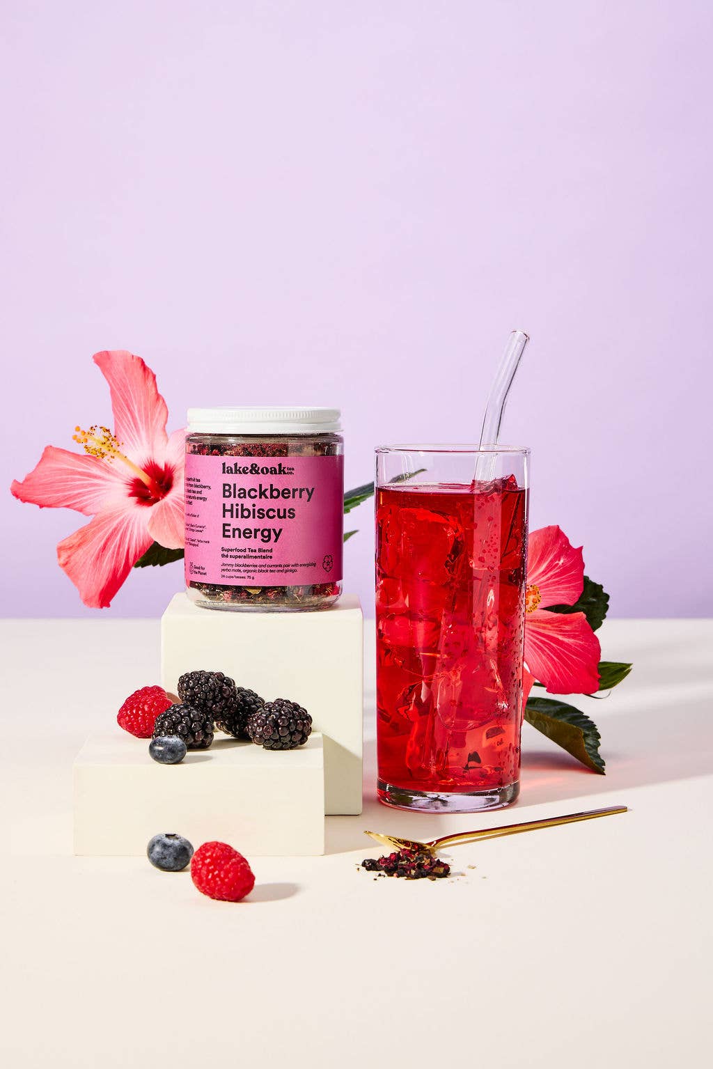 Jar of blackberry hibiscus energy drink mix with a glass of red drink and flowers on a light purple background