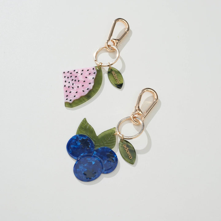 Two keychains shaped like watermelon and blueberries on a light gray background