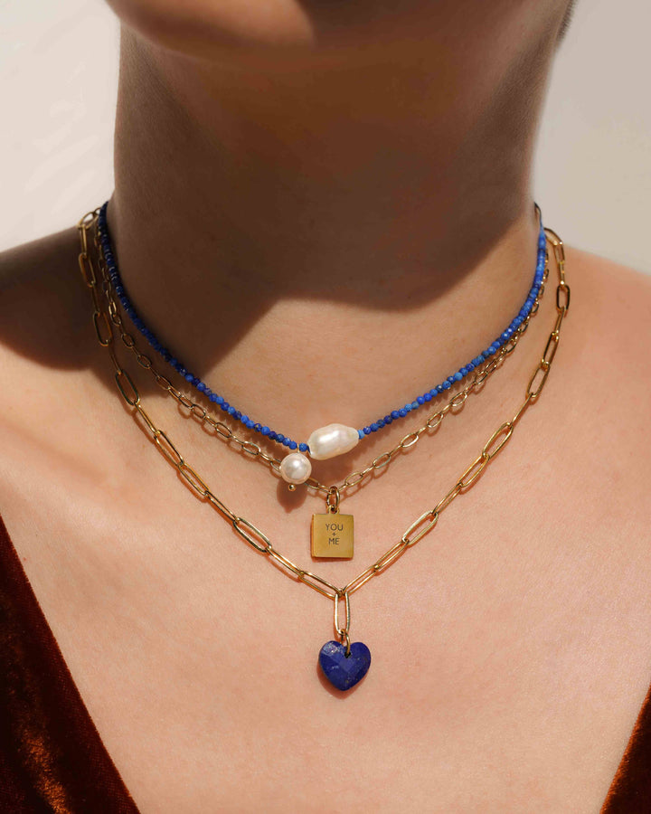 Necklace with blue heart pendant and gold chain on a person's neck