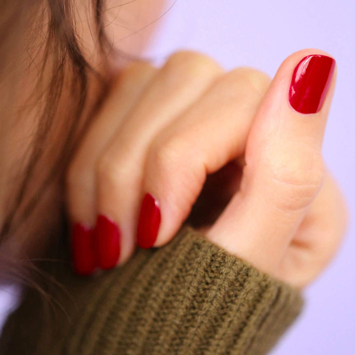 Close-up of a hand with red nail polish wearing a green sweater.