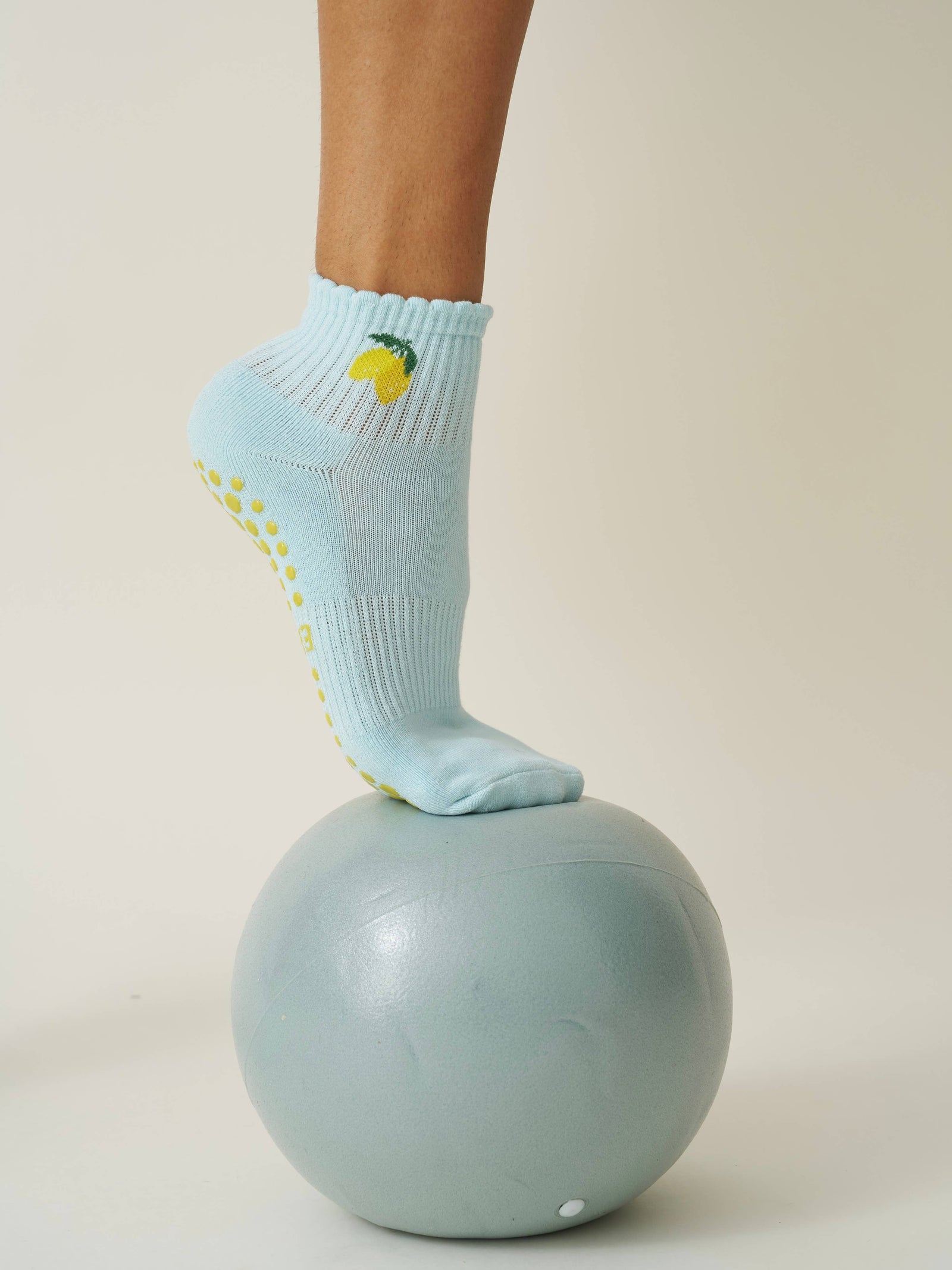 Person wearing Light blue pilates socks with yellow slip-resistant dots and lemon designs on a light gray ball against a beige background