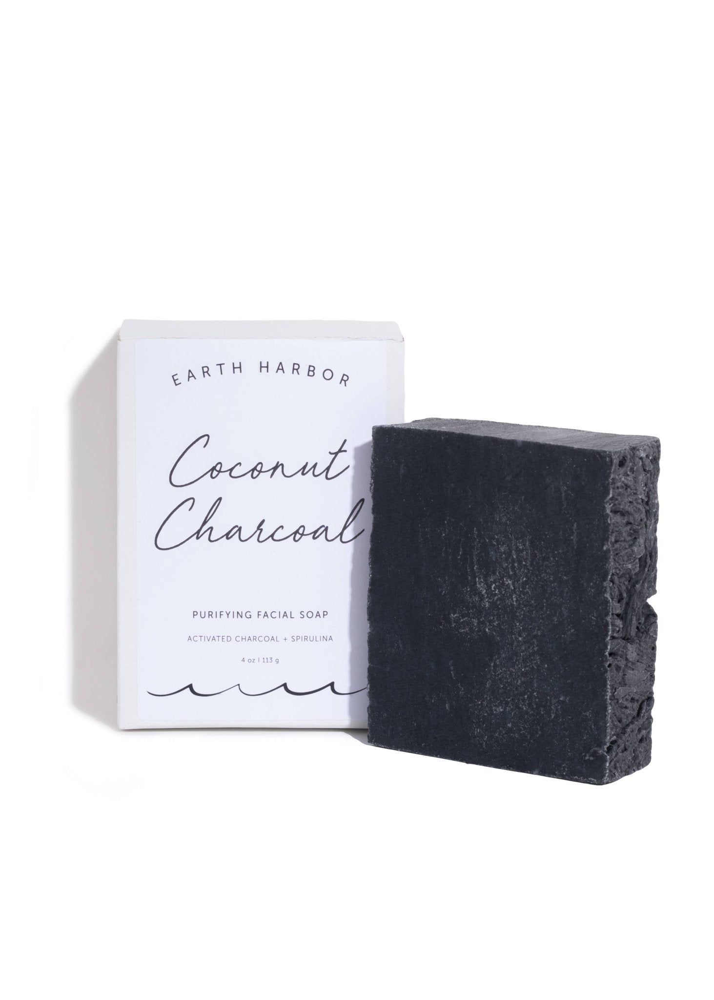 Bar of coconut charcoal soap next to its packaging on a white background