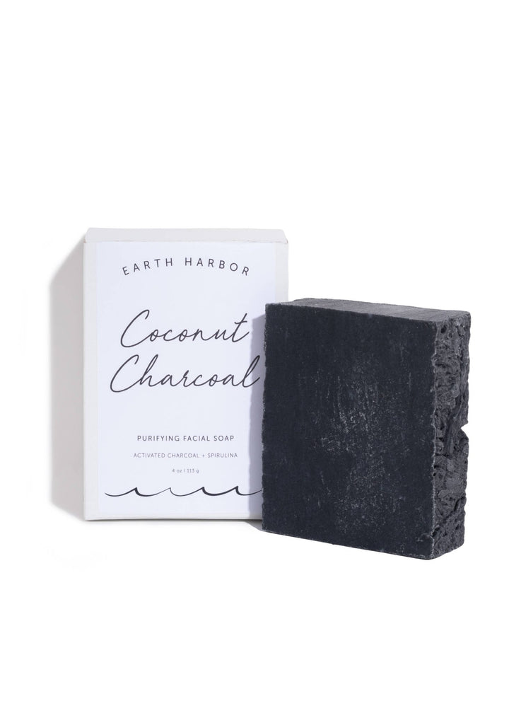 Bar of coconut charcoal soap next to its packaging on a white background