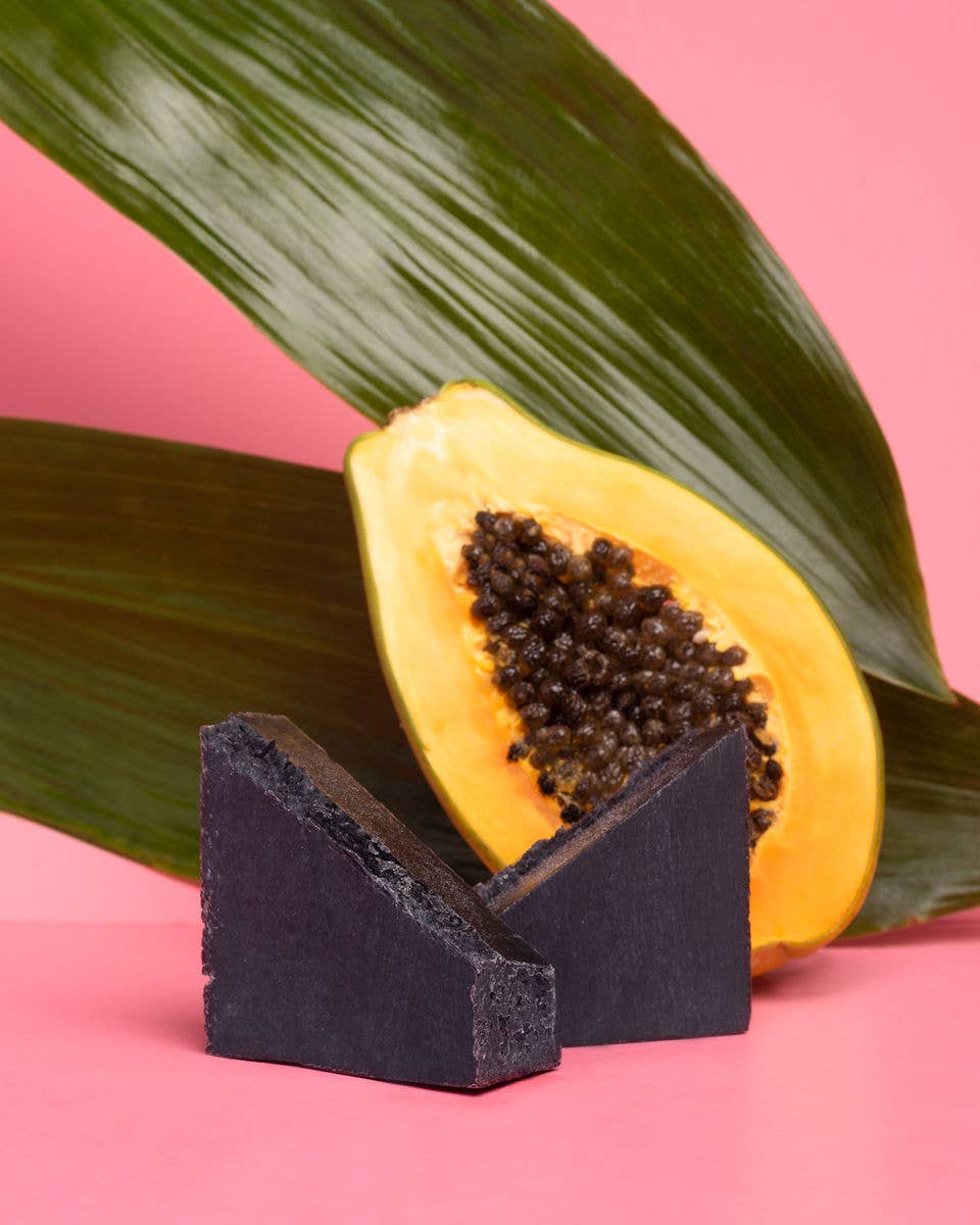 Earth Harbor coconut Charcoal Soap bar with a half-cut papaya on a pink background