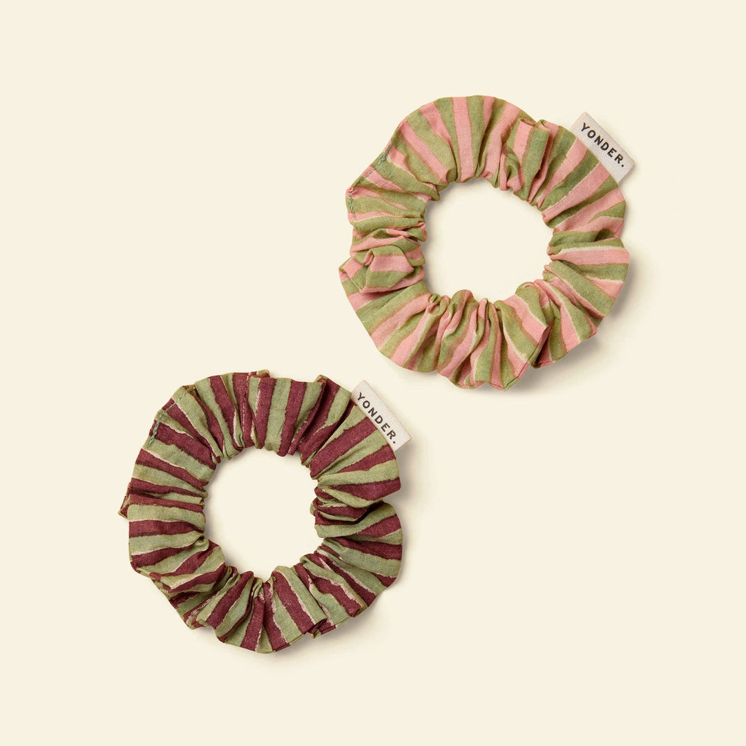 Two fabric scrunchies by yonder on a warm cream background. One scrunchie has vertical pink and sage green stripes, and the other has vertical burgundy and sage green stripes.