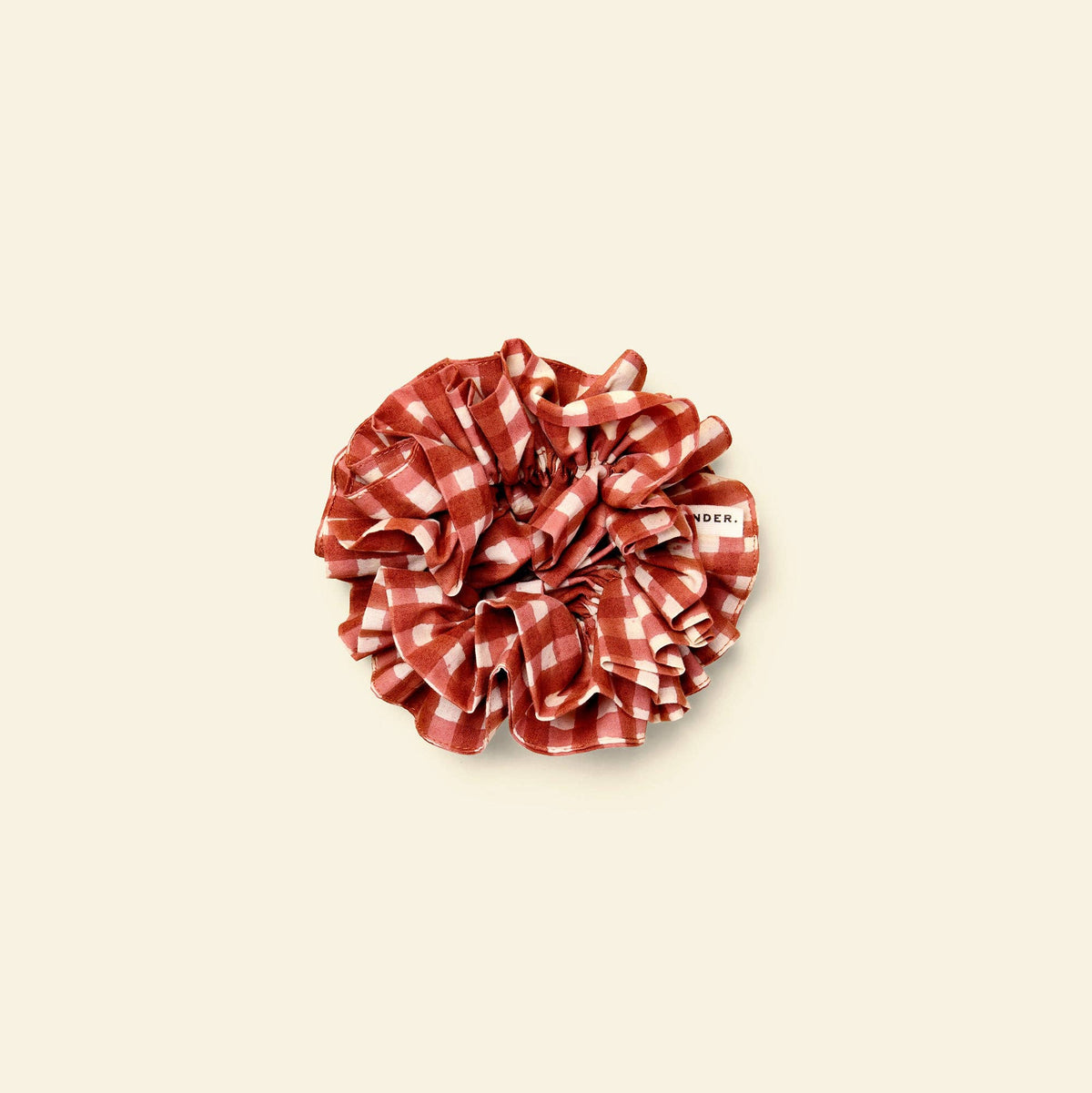 A red and white gingham patterned fabric scrunchie with a small white brand tag reading 'yonder' on the side, centered on a solid cream background.