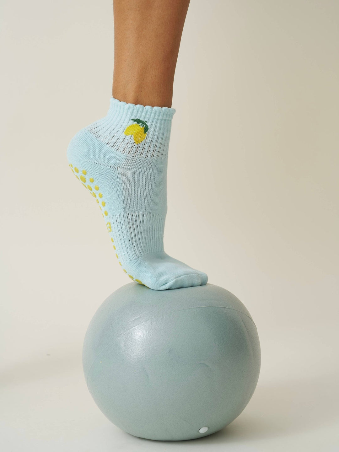 Person wearing Light blue pilates socks with yellow slip-resistant dots and lemon designs on a light gray ball against a beige background