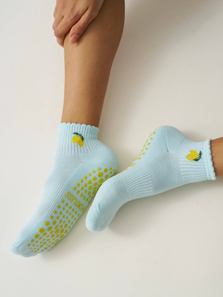 Person wearing light blue pilates socks with yellow slip-resistant dots and lemon designs on a beige background