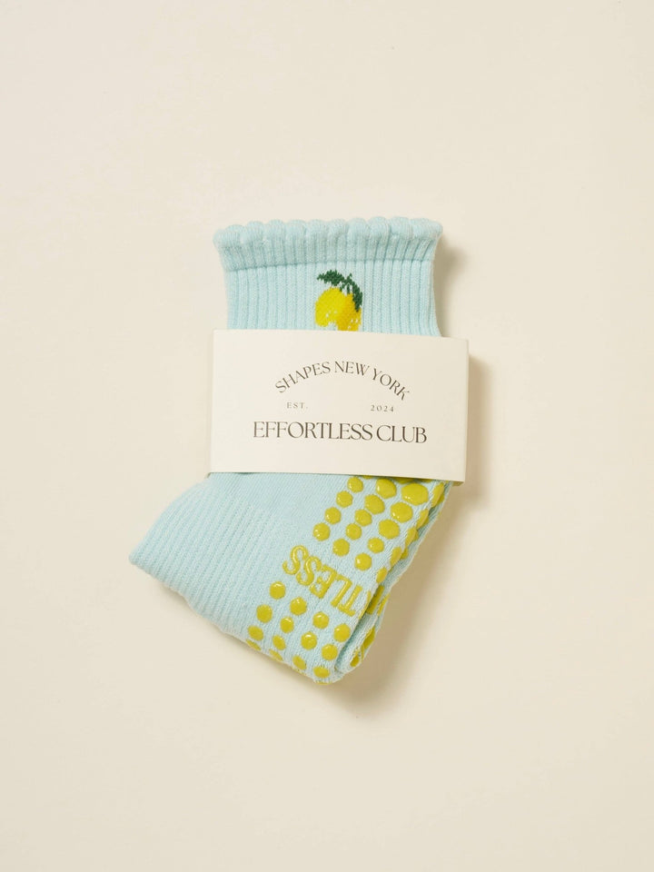 Light blue pilates socks with yellow slip-resistant dots and lemon designs on a beige background