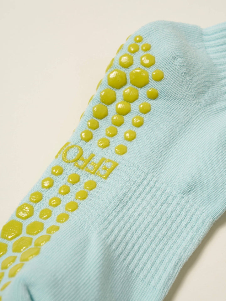 Light blue ankle sock with yellow grip dots on a beige background