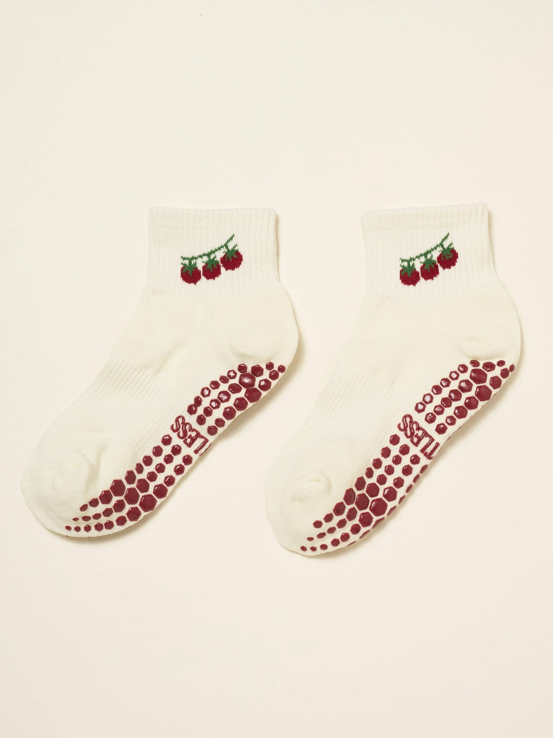 Pair of pilates socks with tomato design and red grips on a beige background
