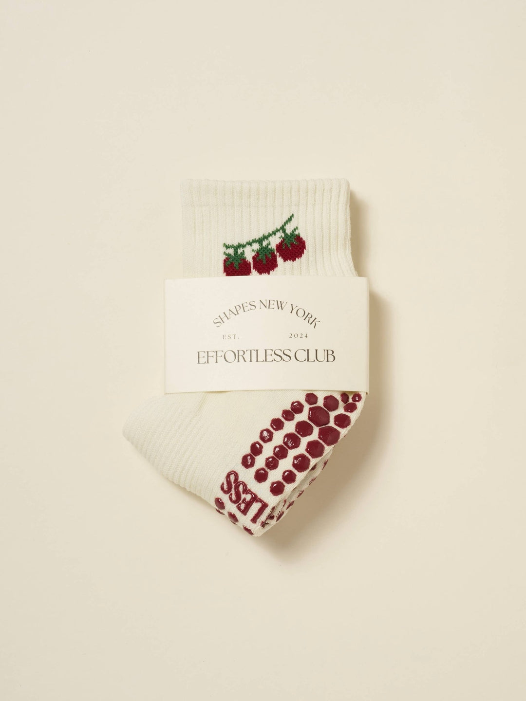 Pair of pilates socks with tomato design and red grips on a beige background