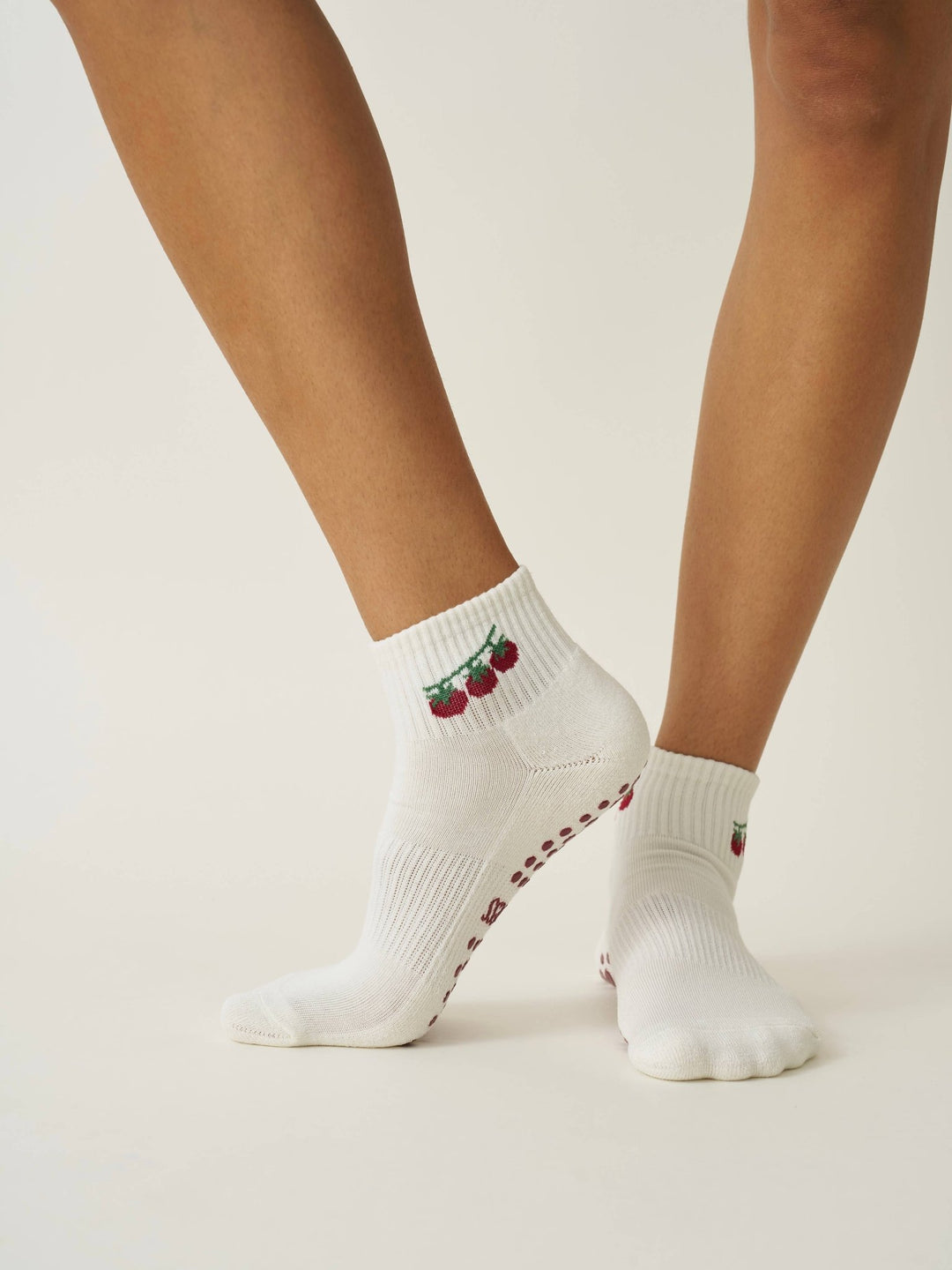 Pair of pilates socks with tomato design and red grips worn by a person on a light background