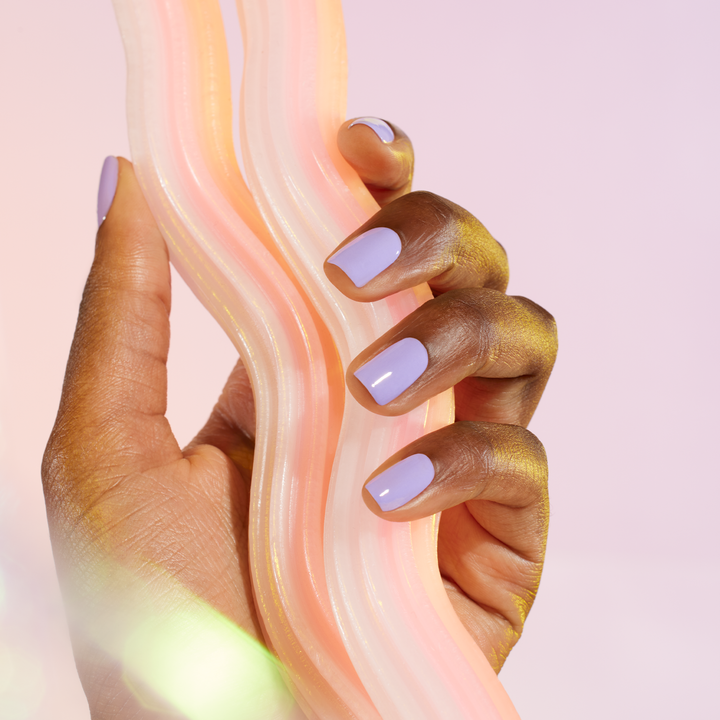Close-up of a hand with wisteria nail polish holding a soft, pastel-colored fabric.