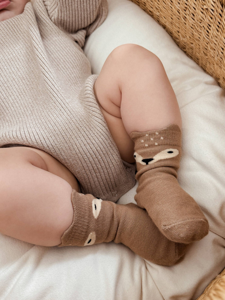 Baby wearing brown socks with animal design on a soft surface