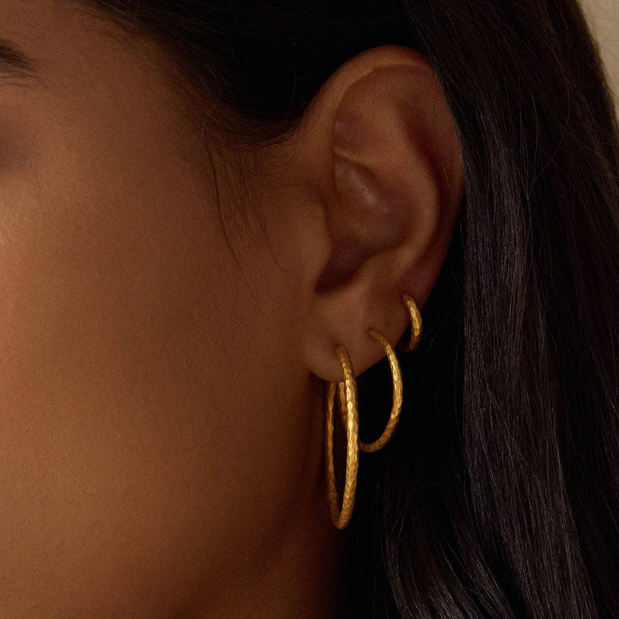 Close-up of an ear wearing gold hoop earrings with dark hair and skin background