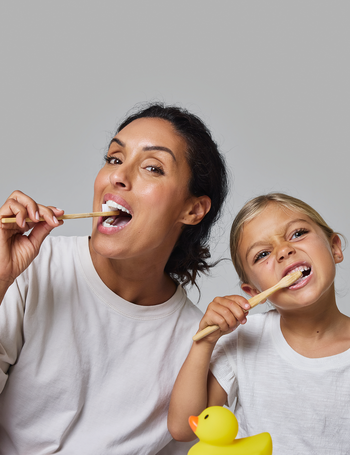 Woman and child brushing their teeth together with a rubber duck on a gray background