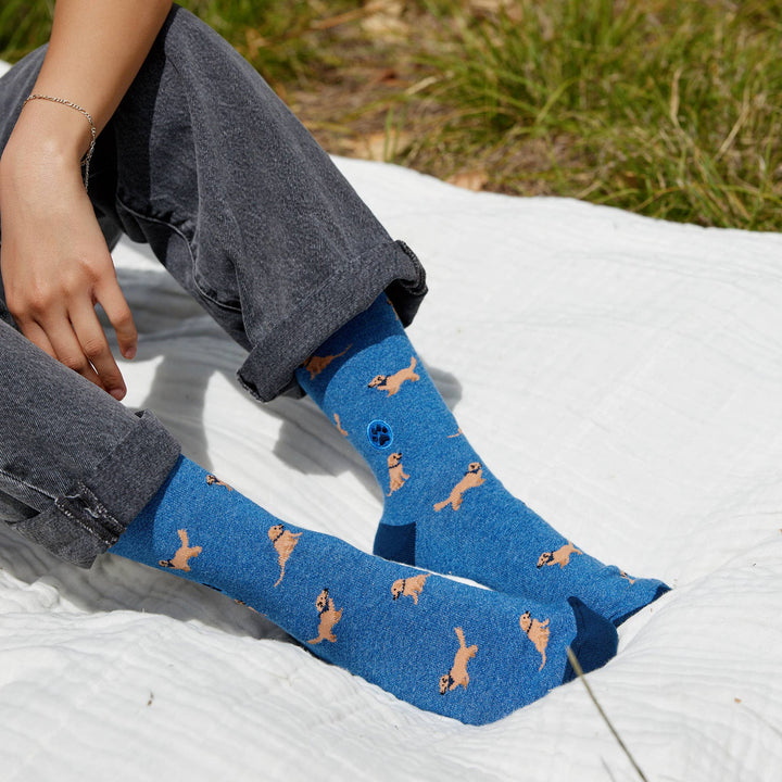 Person wearing blue socks with dog pattern sitting on a white blanket outdoors.