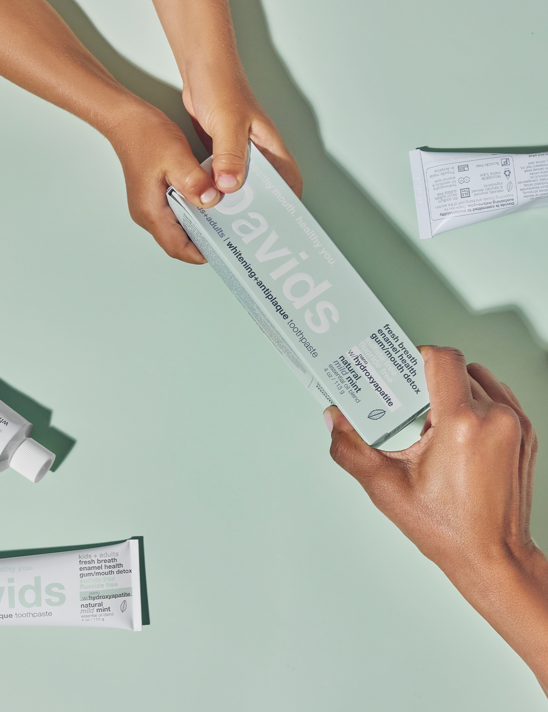 Two hands holding a box of Davids toothpaste on a light green background