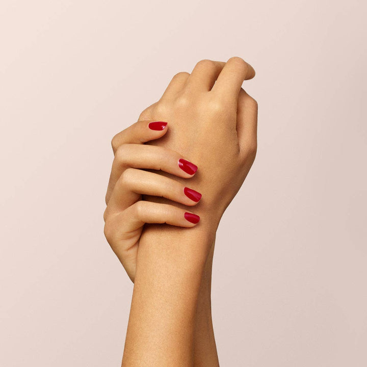 Close-up of a hand with red nail polish on a beige background